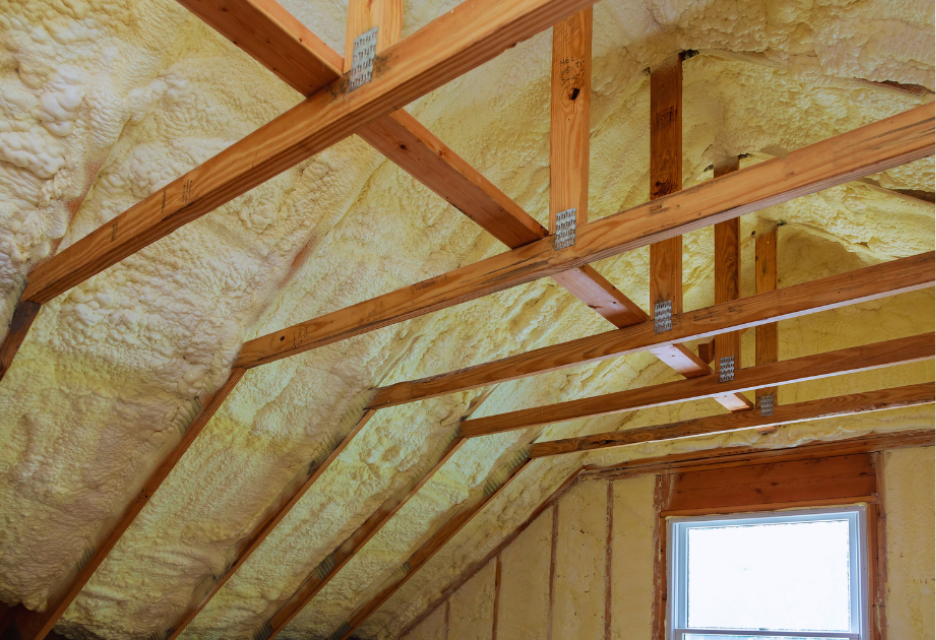 Attic roof and walls insulated with spray foam between exposed wooden framing to improve energy efficiency and prevent winter heat loss.